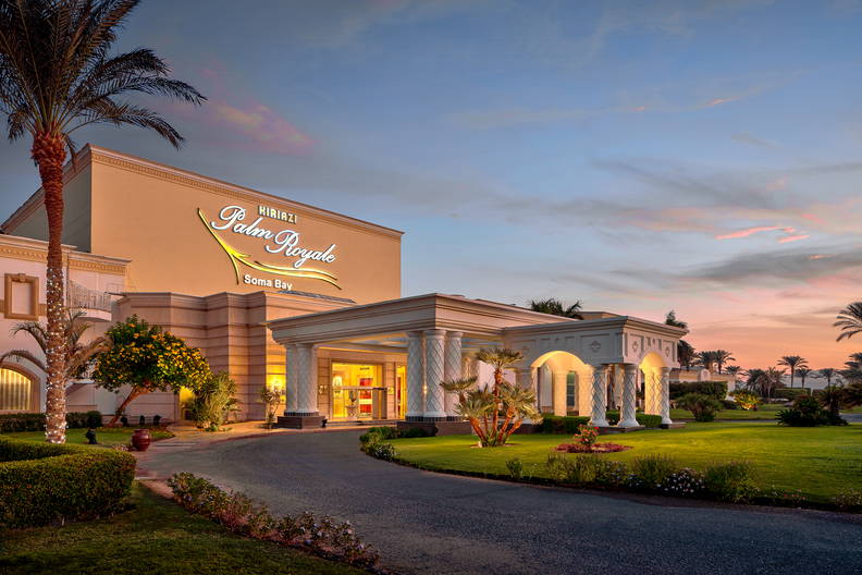 Hotel Palm Royale z podjazdem i palmami o zmierzchu.