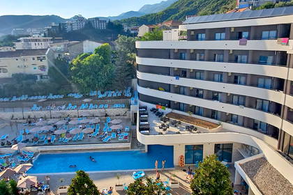 Hotel z basenem i placem zabaw w słoneczny dzień, widok z góry.