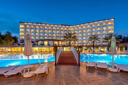 Oświetlony nocą hotel z basenem i mostkiem.