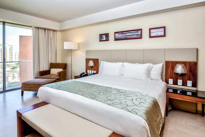 Pokój hotelowy z dużym łóżkiem, balkonem i fotelami wypoczynkowymi.