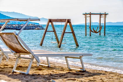 Plaża z leżakami, huśtawką i hamakiem na wodzie.