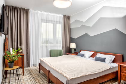 Pokój hotelowy z łóżkiem małżeńskim i dekoracją ścienną o tematyce górskiej.