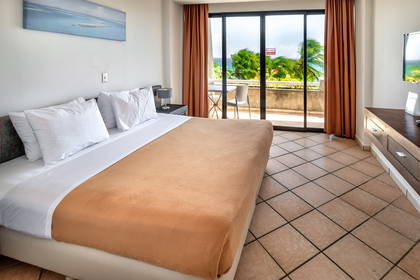 Pokój hotelowy z balkonem i widokiem na tropikalną roślinność.