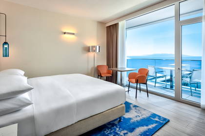 Jasny pokój hotelowy z balkonem i widokiem na morze.
