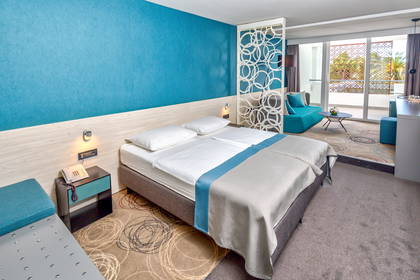Pokój hotelowy z łóżkiem, balkonem i turkusowymi dodatkami.