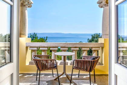 Balkon z widokiem na morze, kolumny, stół i krzesła.