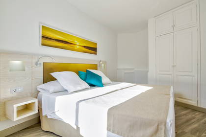 Jasny pokój hotelowy z łóżkiem, szafką nocną i białą szafą.