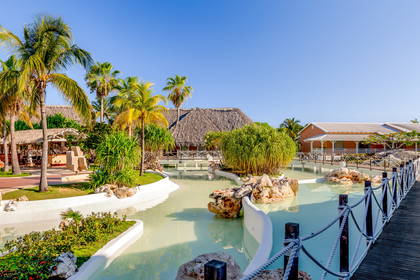 Resort z palmami, wodą i drewnianymi ścieżkami.
