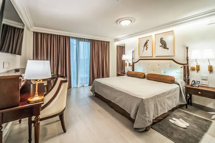 Pokój hotelowy z dużym łóżkiem, biurkiem i brązowymi zasłonami w oknach.