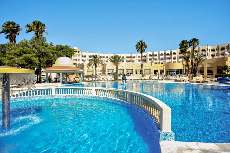 Basen w hotelu z palmami. W tle budynek.