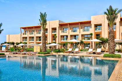 Kompleks hotelowy z basenem, leżakami i palmami.