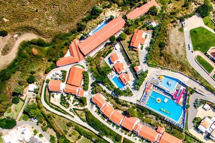 Resort z czerwonymi dachami, basenami i krętą drogą, widok z lotu ptaka.