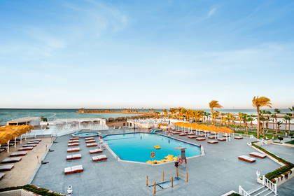 Widok z góry na hotelowy basen, morze i plażę z palmami.