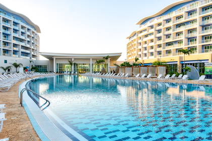 Basen otoczony budynkami hotelowymi i leżakami.