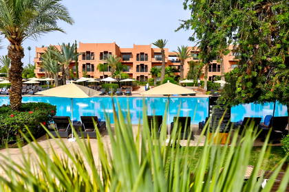 Hotel z basenem, leżakami i palmami.