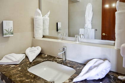 Nowoczesna łazienka hotelowa z marmurowym blatem, umywalką, szklankami i starannie złożonymi białymi ręcznikami.