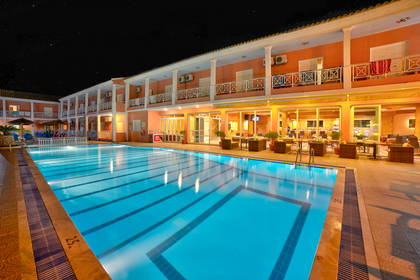 Oświetlony basen hotelowy nocą. W tle budynek.