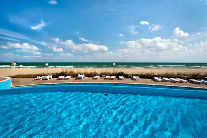 Błękitny basen z widokiem na plażę i leżakami.