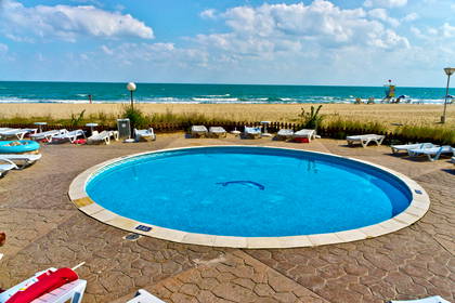 Okrągły basen na piaszczystej plaży, w tle morze.