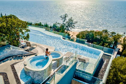 Kobieta relaksuje się w jacuzzi z widokiem na basen i ocean. Zdjęcie z góry.