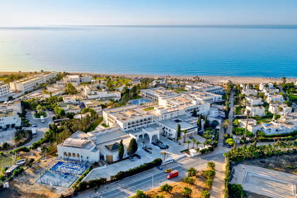 Hotel w jasnych barwach przy piaszczystej plaży, widok z góry.