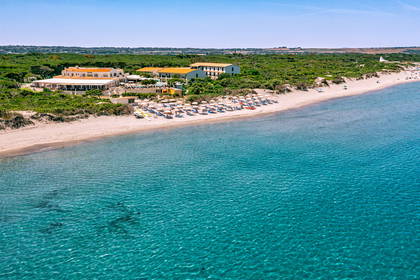Hotel przy plaży z parasolami, turkusowa woda widziana z lotu ptaka.