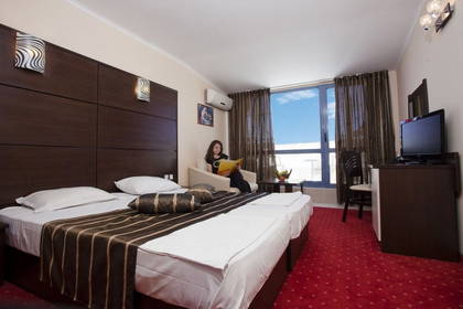 Kobieta czyta książkę w fotelu w pokoju hotelowym.