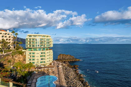 Hotel z basenem nad oceanem, błękitne niebo w tle.