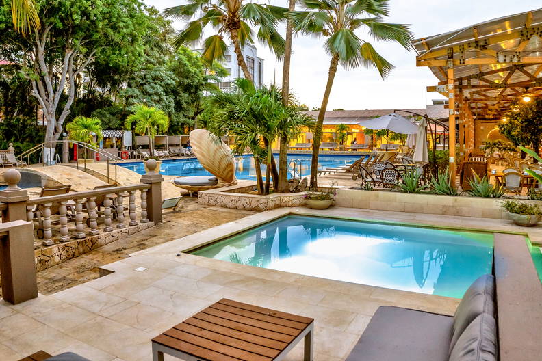 Kompleks basenowy z palmami i restauracją w tle.