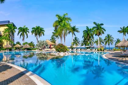 Panorama basenu z palmami i budynkami hotelowymi w tle.
