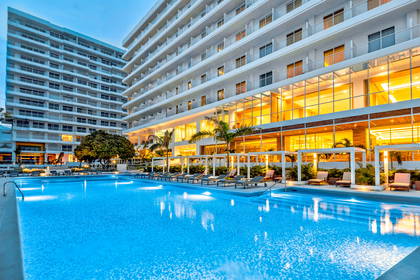 Basen hotelowy z leżakami i budynkami w tle.
