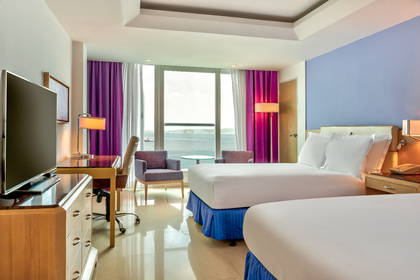 Pokój hotelowy z dwoma łóżkami, biurkiem i widokiem na ocean.