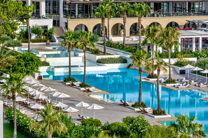 Luksusowy hotel z dużym basenem otoczonym palmami, leżakami i białymi parasolami.