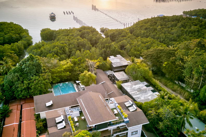 Hotel otoczony zielenią widziany z góry. W tle morze, łodzie i zachód słońca.