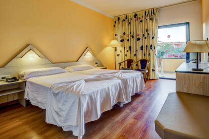 Pokój hotelowy z dwoma łóżkami, balkonem i widokiem na palmy.