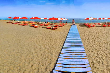 Plaża z czerwonymi parasolami i niebieską, drewnianą ścieżką.