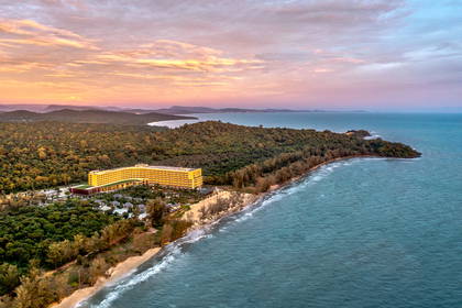 Żółty hotel na plaży widziany z góry. W tle las i morze.