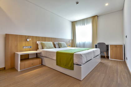 Jasny pokój hotelowy z łóżkiem, biurkiem i drewnianą podłogą.