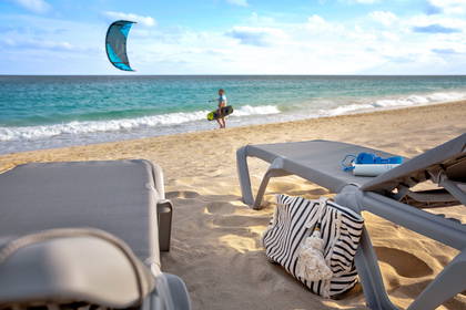 Plaża z leżakami, torbą i kitesurferem na wodzie w tle.