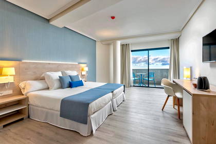 Jasny pokój hotelowy z balkonem i widokiem na morze.