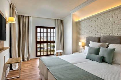 Pokój hotelowy z podwójnym łóżkiem, oknem i ścianą z cegły.