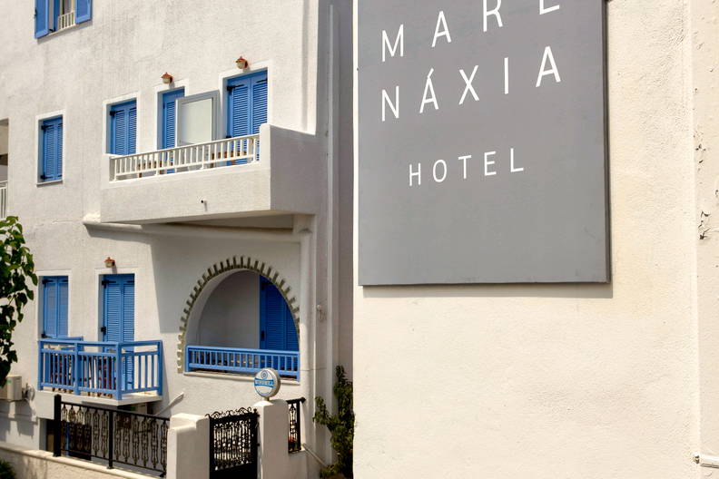 Biały budynek hotelu z niebieskimi okiennicami i szyldem „Mare Naxia Hotel”.