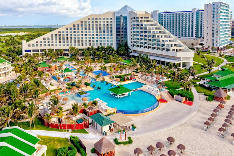 Kompleks hotelowy z basenami, palmami i plażą, widok z góry.