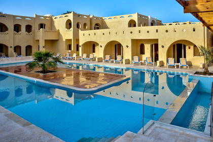 Basen hotelowy z leżakami i budynkiem w tle.