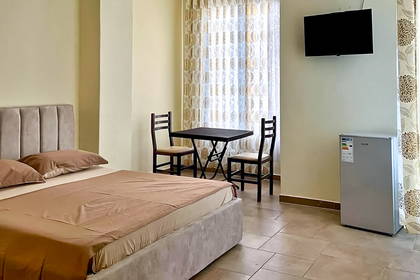 Pokój hotelowy z łóżkiem, stolikiem, telewizorem i małą lodówką.