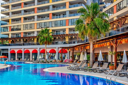Kompleks hotelowy z basenem, leżakami i palmami.