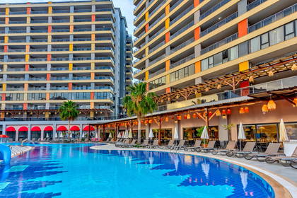 Kompleks hotelowy z basenem i leżakami. W tle budynki.