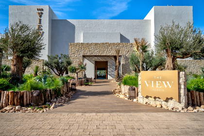 Wejście do hotelu The View Agadir z kamienną fasadą i drewnianym chodnikiem.