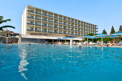 Hotel z basenem. Ludzie pływają i odpoczywają na leżakach.