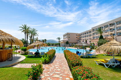 Hotel z basenem, leżakami i palmami.